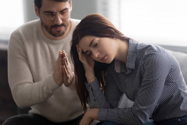 A couple sitting together after an argument, with one partner leaning forward and resting her head in her hand.